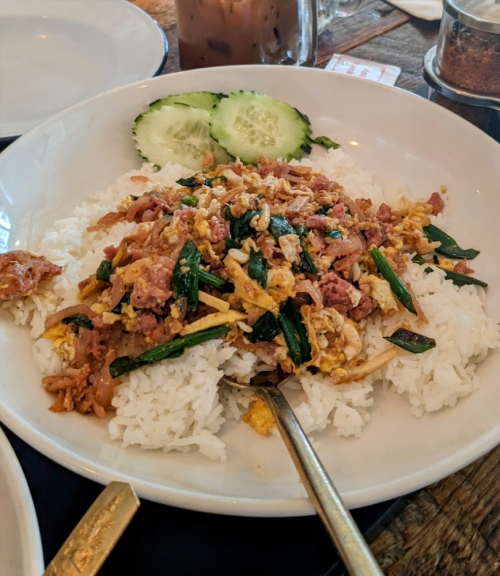 A plate of rice topped with stir-fried meat, vegetables, and egg, garnished with cucumber slices.